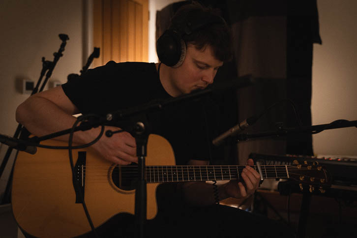 Kelvin playing recording acoustic guitar in dark bedroom music room
